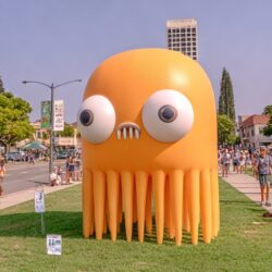 Giant orange inflatable octopus character on a street festival lawn with a crowd walking past