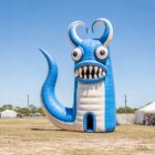 inflatable-walk-in-monster-festival-entrance Blue horned inflatable monster with a walk-in doorway at an outdoor festival