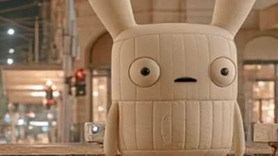 Concept image: a three-metre matte inflatable character on a wet Melbourne street at night, tram wires overhead and projectors on stands