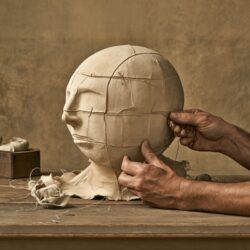 A maker stitching fabric panels onto a mascot head form on a workbench